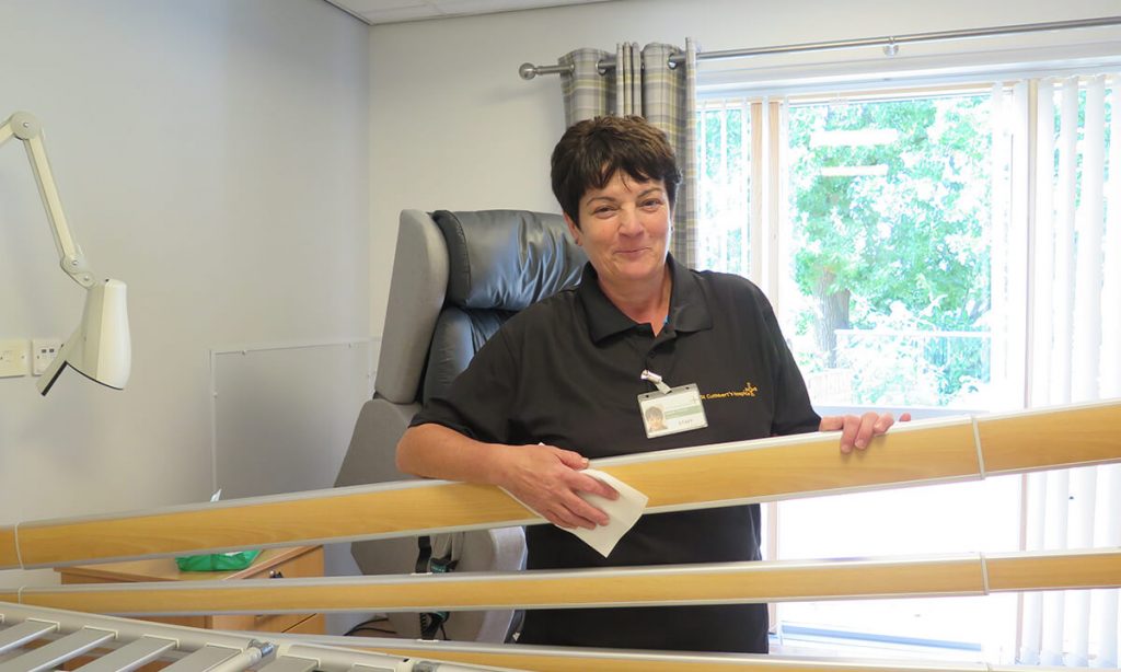 A lady stands with a cleaning cloth next to a bed rail