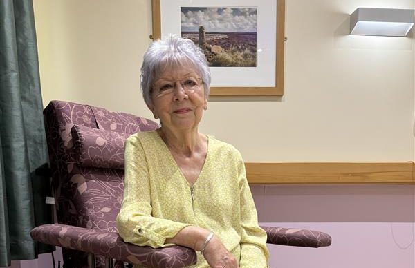 Elaine sitting in chair, a picture in a frame behind her. Looking content.