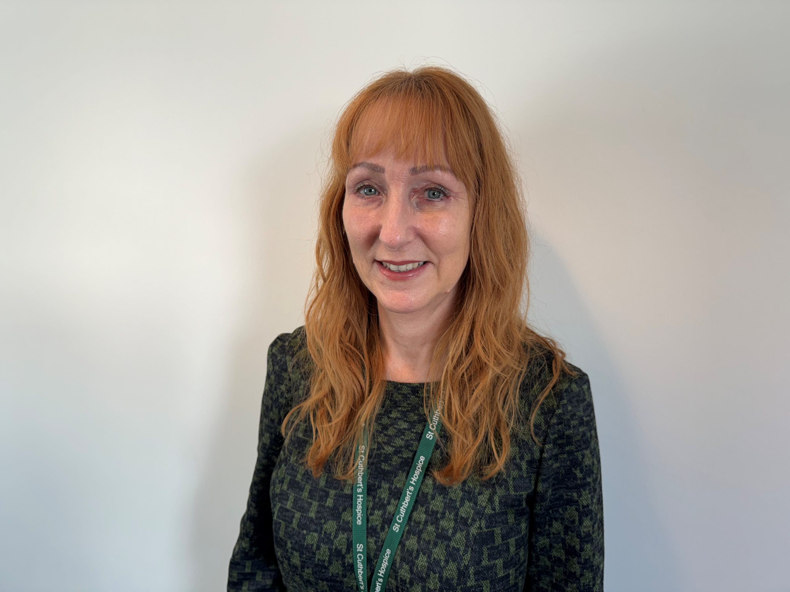 A woman with vibrant red hair wearing a green lanyard smiles toward the camera.