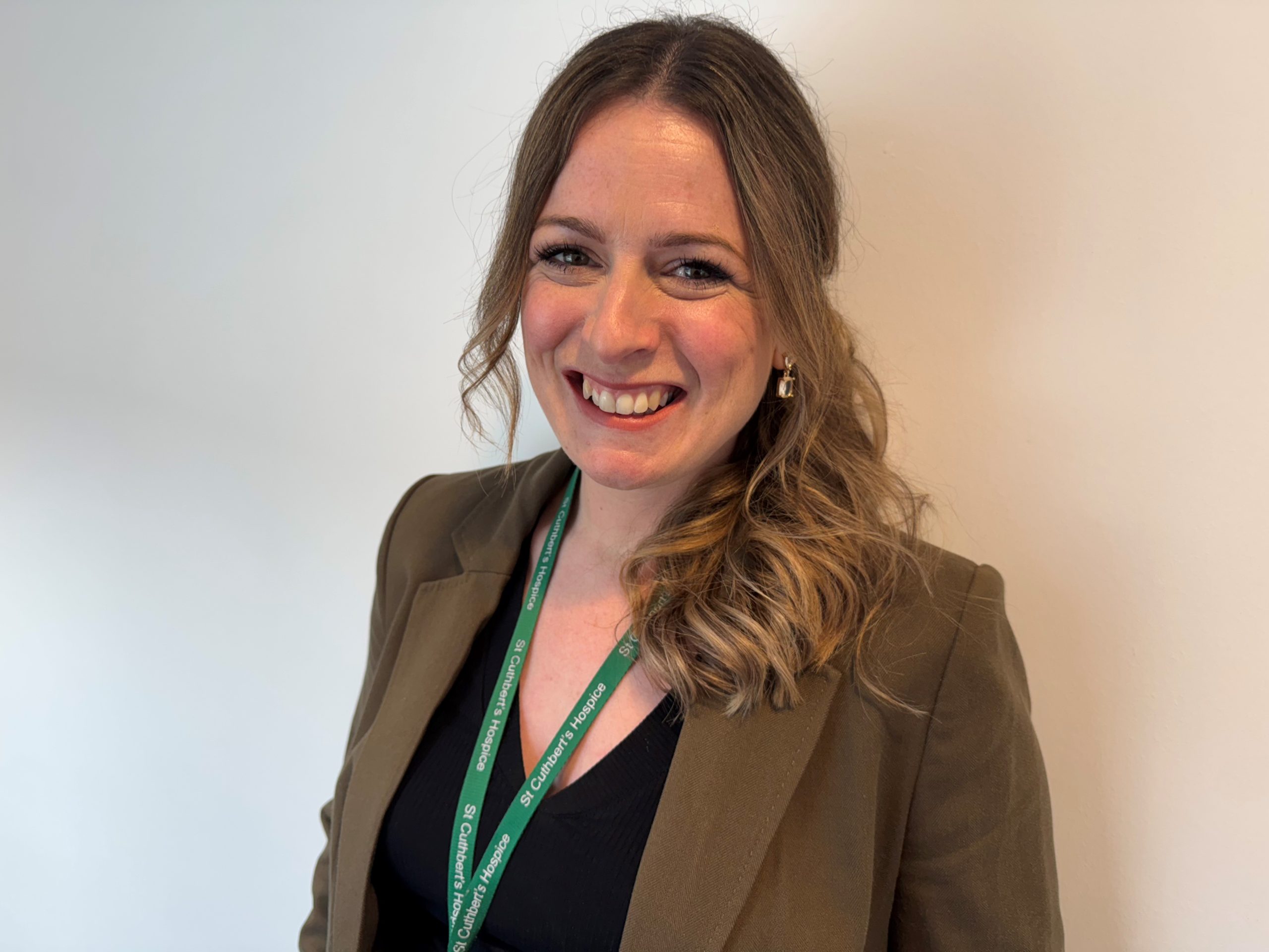 1. A woman in a suit wearing a green lanyard smiles confidently at the camera.